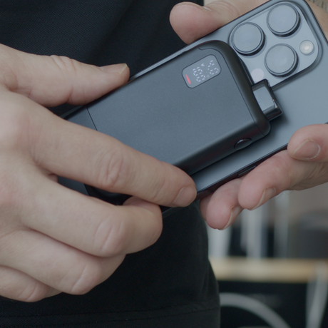 Hands holding an iPhone with MagBox Magnetic 510 Battery attached on the back, displaying a digital charge readout, showcasing sleek design and magnetic convenience.