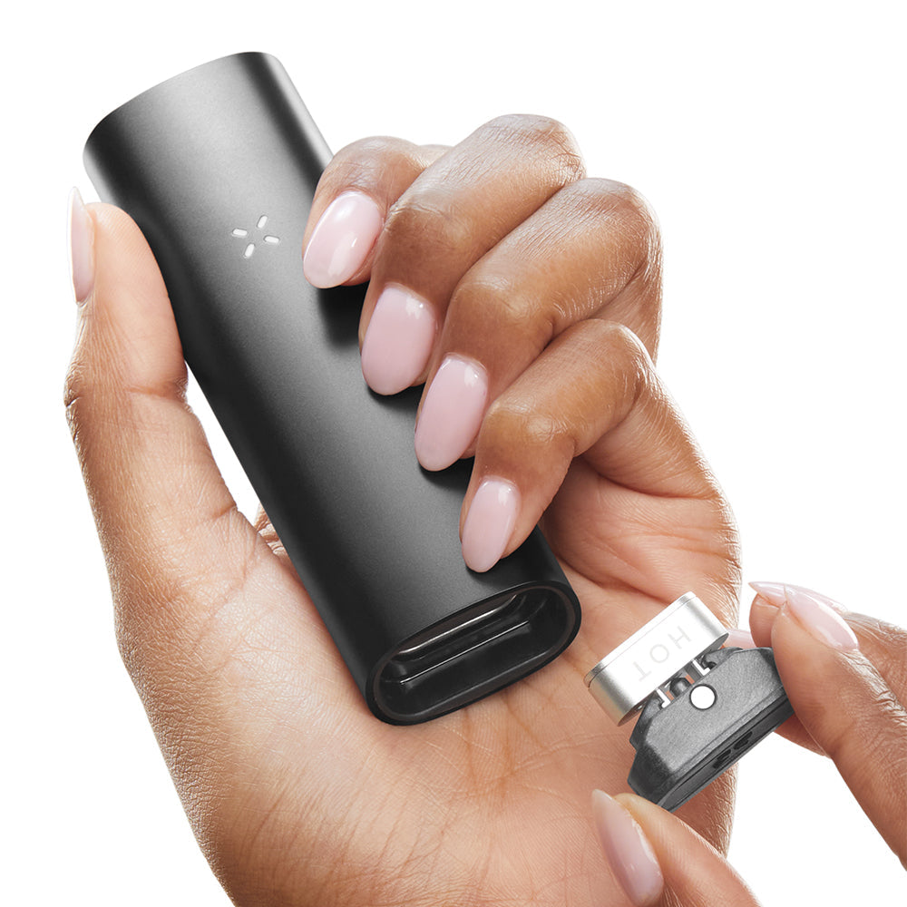Hands holding PAX 3 Complete Kit - Onyx, showcasing the matte black battery unit and removable metal/ceramic heating chamber for vaporizing dry herbs and concentrates.