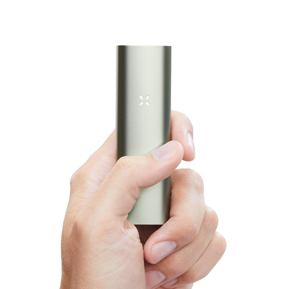Hand holding a slim, metallic PAX 3 Basic Kit vaporizer with an X-shaped LED indicator, showcasing its sleek, polished design and portability.