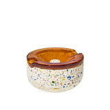Symi Ashtray with terrazzo base and amber-tinted glass insert, featuring built-in cigarette rests and integrated grooves for functionality.