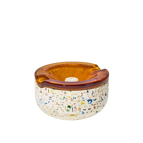 Symi Ashtray with terrazzo base and amber-tinted glass insert, featuring built-in cigarette rests and integrated grooves for functionality.