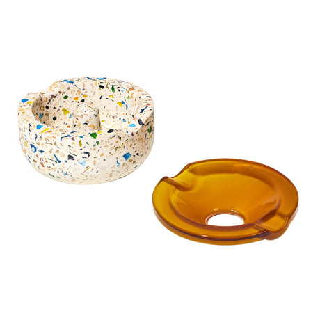 Symi Ashtray featuring a terrazzo concrete base with colorful flecks beside an amber borosilicate glass top, each with cigarette notches.
