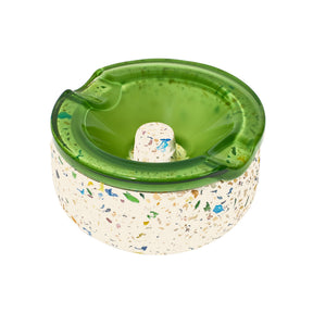 Symi Ashtray with a terrazzo concrete base and removable translucent green borosilicate glass top featuring cigarette grooves and a central raised knob.