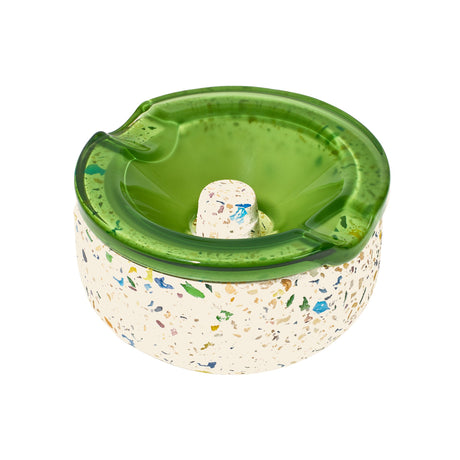 Symi Ashtray with a terrazzo concrete base and removable translucent green borosilicate glass top featuring cigarette grooves and a central raised knob.