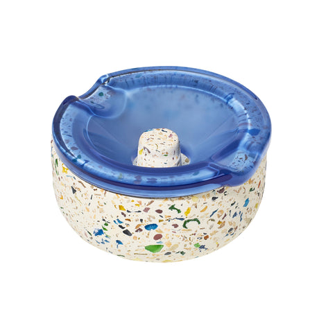 Symi Ashtray featuring a terrazzo-style concrete base with a swirled-blue glass insert, notched for cigarettes, highlighting its vintage-modern design.