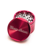 4-piece Aluminum Grinder 2.5 in bright red, showing sharp teeth and multi-chamber design, with the lid engraved Blazy Susan set aside.