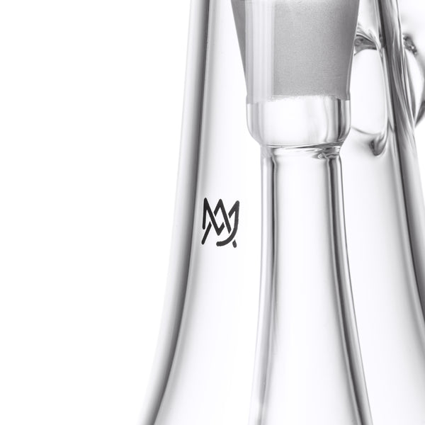 Close-up of the Lumina - Clear, a borosilicate glass bubbler with a cylindrical chamber, frosted joint, and stylized “M” logo, featuring a 4-slot percolator.