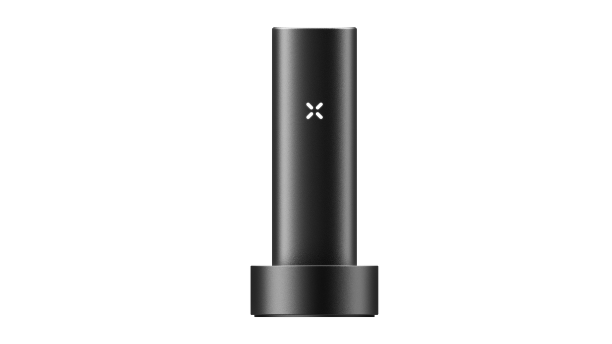 PAX FLOW vaporizer in matte-black, cylindrical design, resting in a round dock, featuring an illuminated “X” logo, highlighting its sleek, portable build.