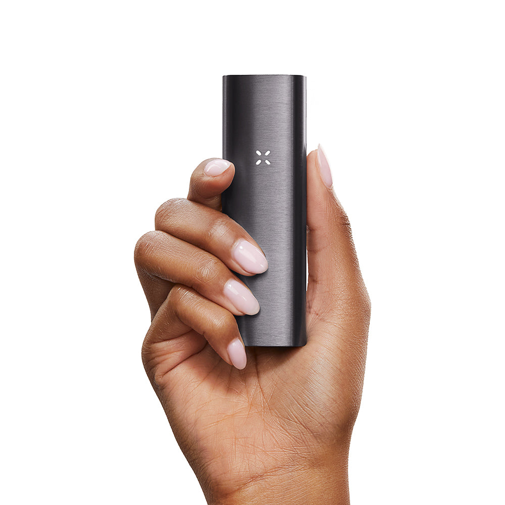 Hand holding the PAX 2 Dry Herb Vaporizer, a sleek, rectangular device with an X-shaped LED indicator on its dark metal finish.