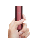 Hand holding the PAX 3 Basic Kit, a sleek red-metallic dry-herb vaporizer with LED indicator, showcasing its portable, stylish design.