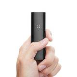 Hand holds PAX 3 Complete Kit - Onyx, a sleek, matte-black vaporizer with LED X indicator, designed for dry herbs and concentrates.