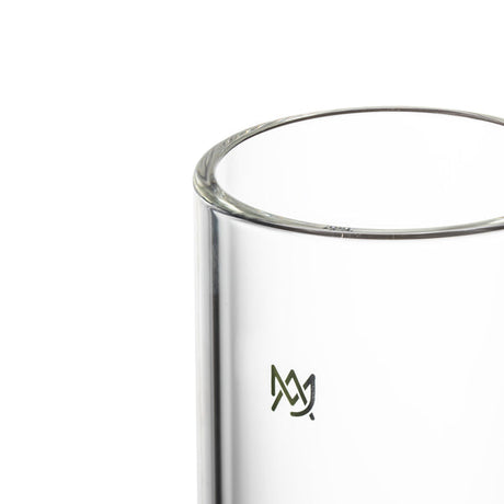 Close-up of an empty double-walled glass tumbler with a small logo, representing the MJ Arsenal Piston Gravity Bong, showcasing its innovative borosilicate glass design.