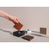 Hand holding Briq Concrete Ashtray with Walnut Lid, showcasing its unique spiral interior design, inspired by M.C. Escher's art, crafted from concrete.