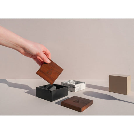 Hand holding Briq Concrete Ashtray with Walnut Lid, showcasing its unique spiral interior design, inspired by M.C. Escher's art, crafted from concrete.