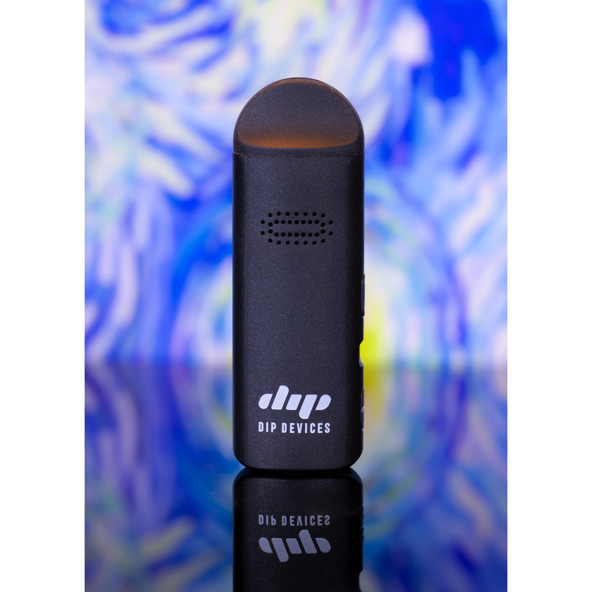 Aster Flower Vaporizer by Dip Devices, a matte black, pocket-sized unit, upright on a reflective surface, showing logo, intake holes, and sleek design.