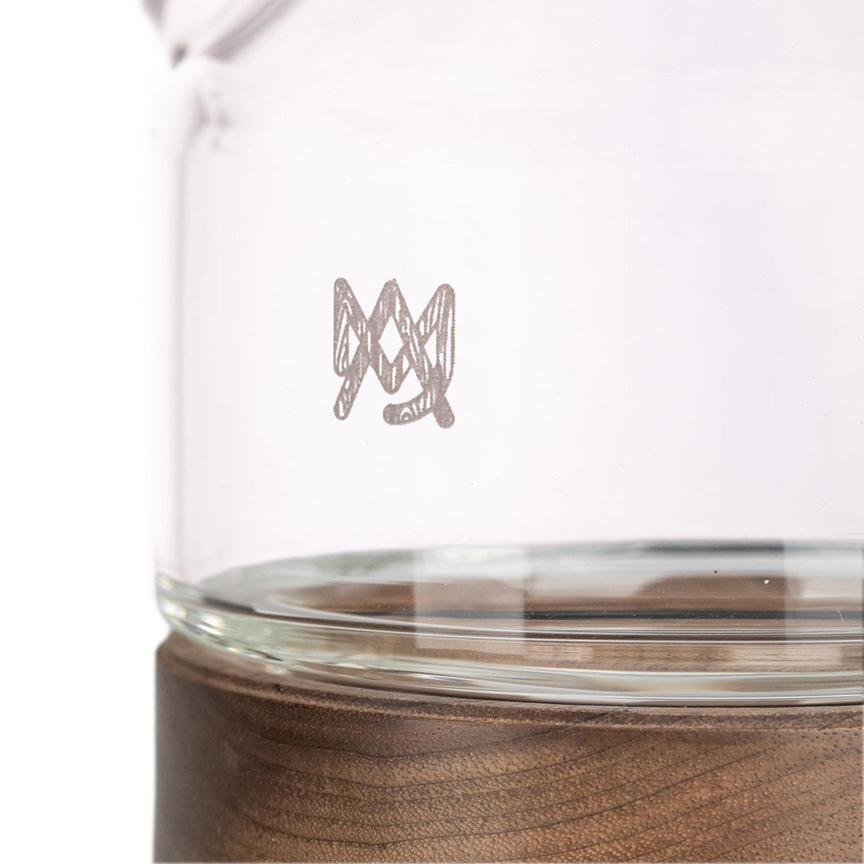 Palisade Bong - Alpine Collection: Close-up of a clear glass vessel with hand-sketched logo, resting on a wooden base, showcasing elegant design and craftsmanship.