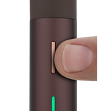A thumb presses the copper button on the Puffco Pivot Electric Dab Pen, highlighting its slim green LED strip and compact design.