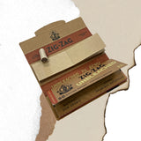 Unbleached 1 1/4 Papers & Tips box with visible logo and rolled cigarette on a white surface, showcasing natural gum Arabic and ultra-thin design.