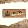 1 1/4 Unbleached Rolling Paper box featuring Zig-Zag logo, natural fibers, slow-burning, ultra-thin, 50 papers per booklet, eco-friendly packaging.